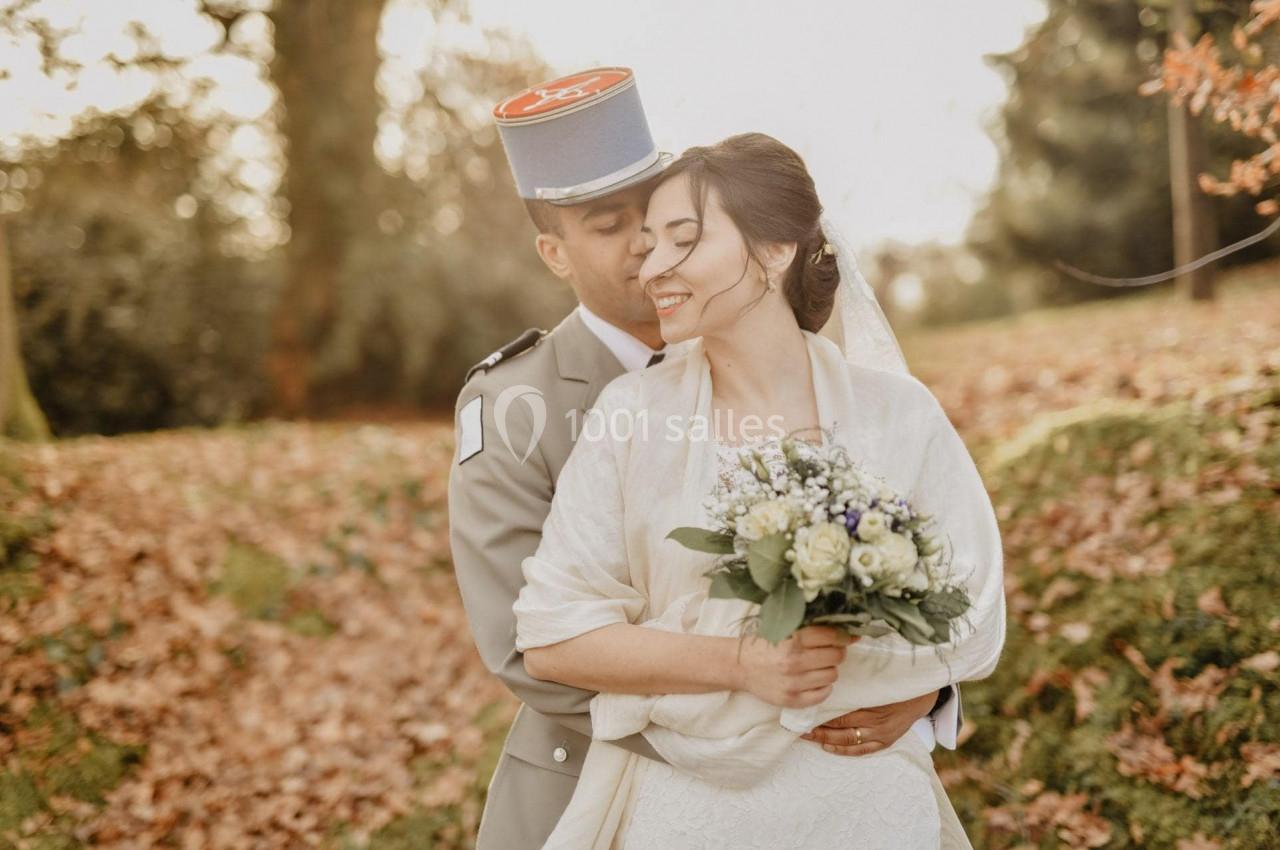 Un couple en tenue de mariage pose dans un parc automnal, le marié en uniforme militaire embrassant la mariée.