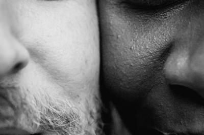 Un couple assis lors d'une cérémonie, l'homme ému essuie une larme tandis que la femme le regarde avec tendresse.