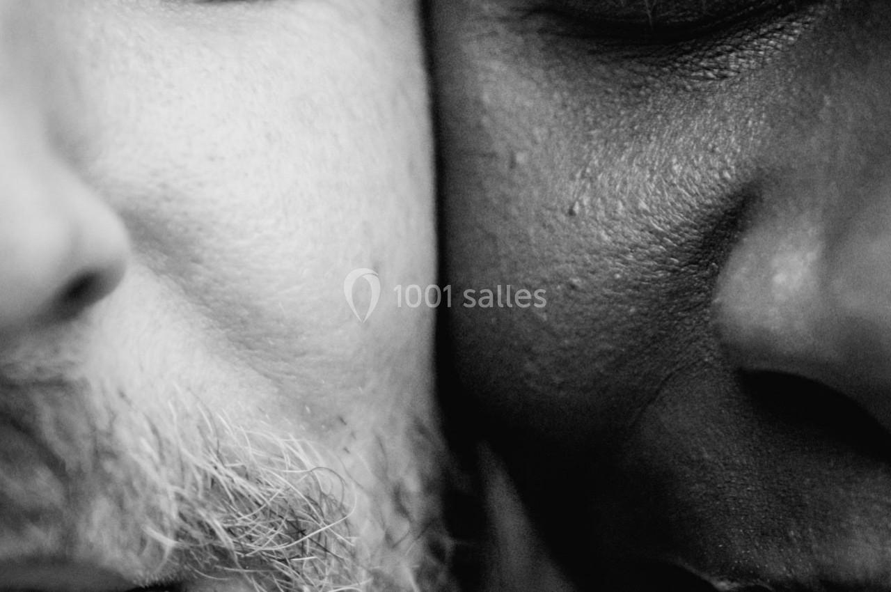 Gros plan en noir et blanc sur les visages partiels d'un homme barbu et d'une femme, leurs regards tournés vers l'objectif.