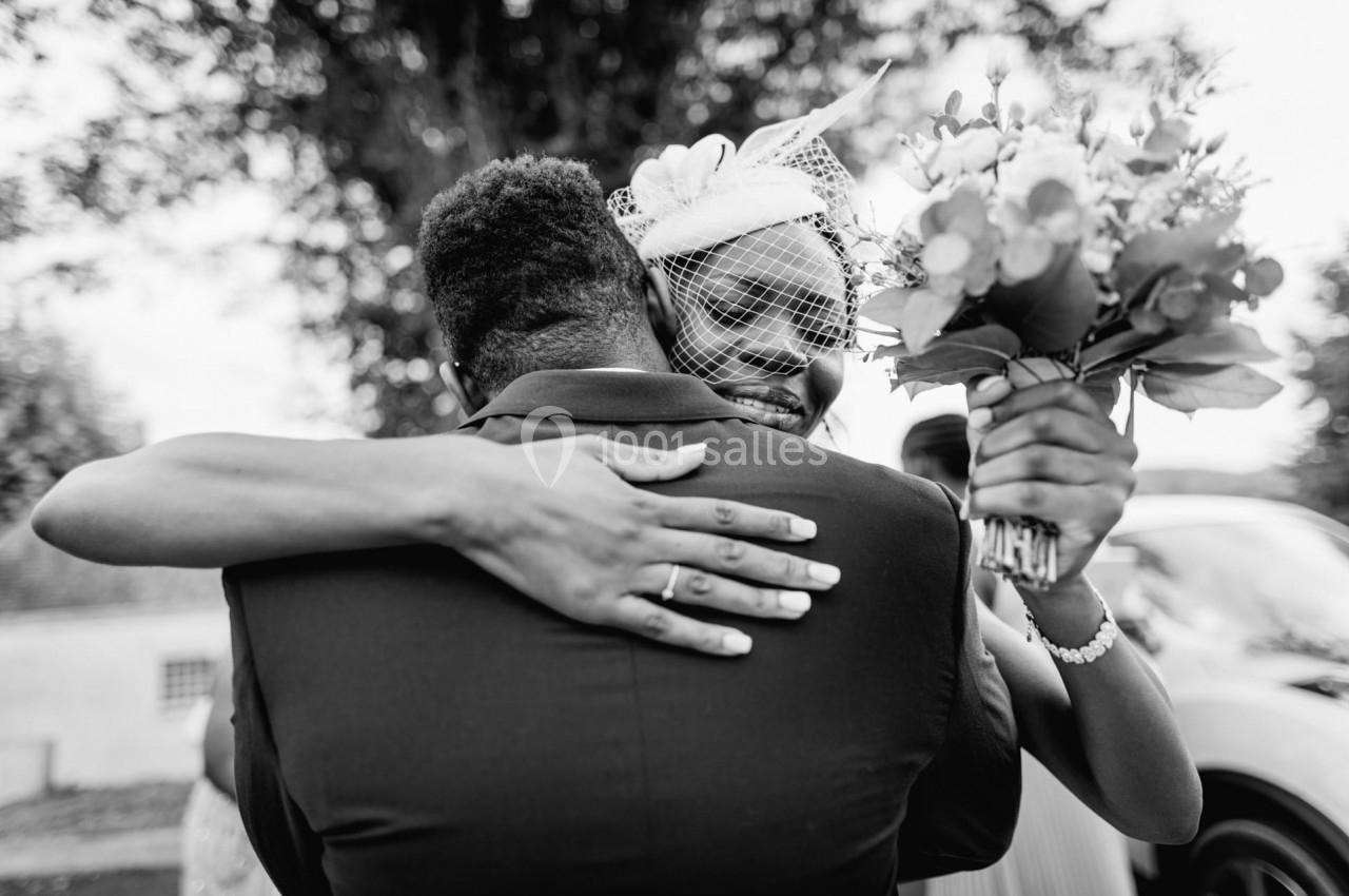 Deux personnes s'enlacent chaleureusement lors d'un événement, une femme tenant un bouquet de fleurs.
