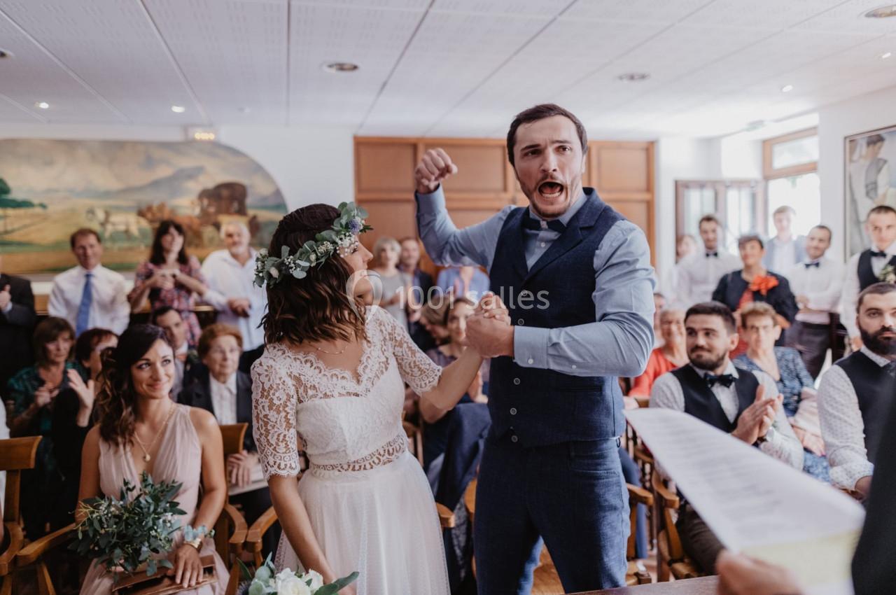 Un couple célèbre son mariage dans une salle avec des invités applaudissant en arrière-plan.