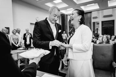 Un couple assis lors d'une cérémonie, l'homme ému essuie une larme tandis que la femme le regarde avec tendresse.