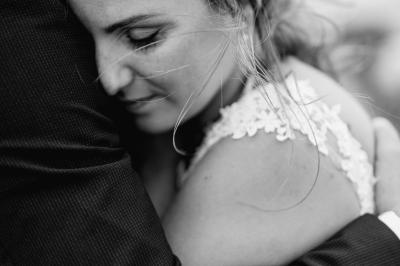 Un couple assis lors d'une cérémonie, l'homme ému essuie une larme tandis que la femme le regarde avec tendresse.