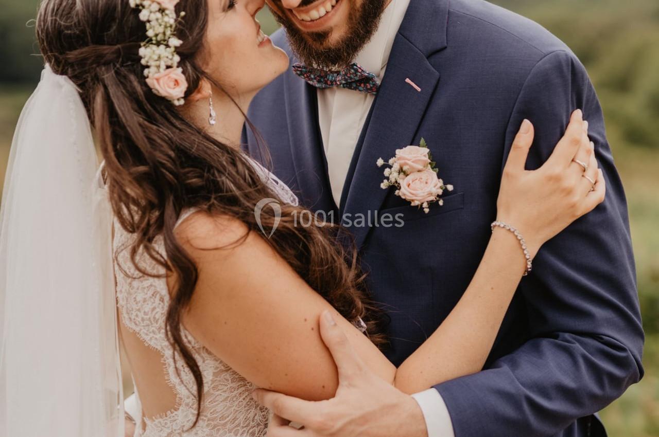 Un couple en tenue de mariage s'enlace tendrement en extérieur, avec un paysage naturel en arrière-plan.