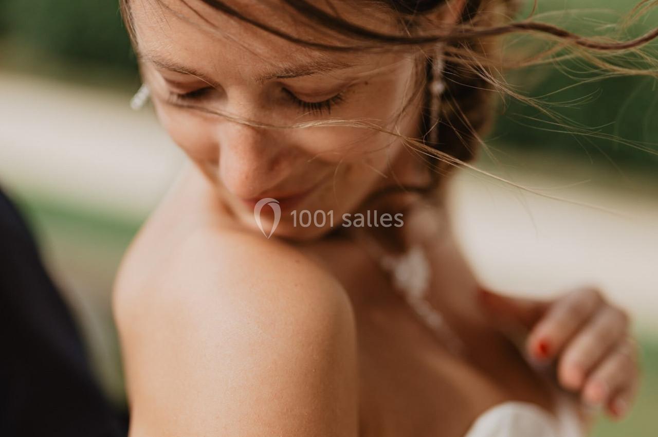 Femme en robe blanche regardant son épaule, cheveux légèrement décoiffés par le vent, arrière-plan flou verdoyant.