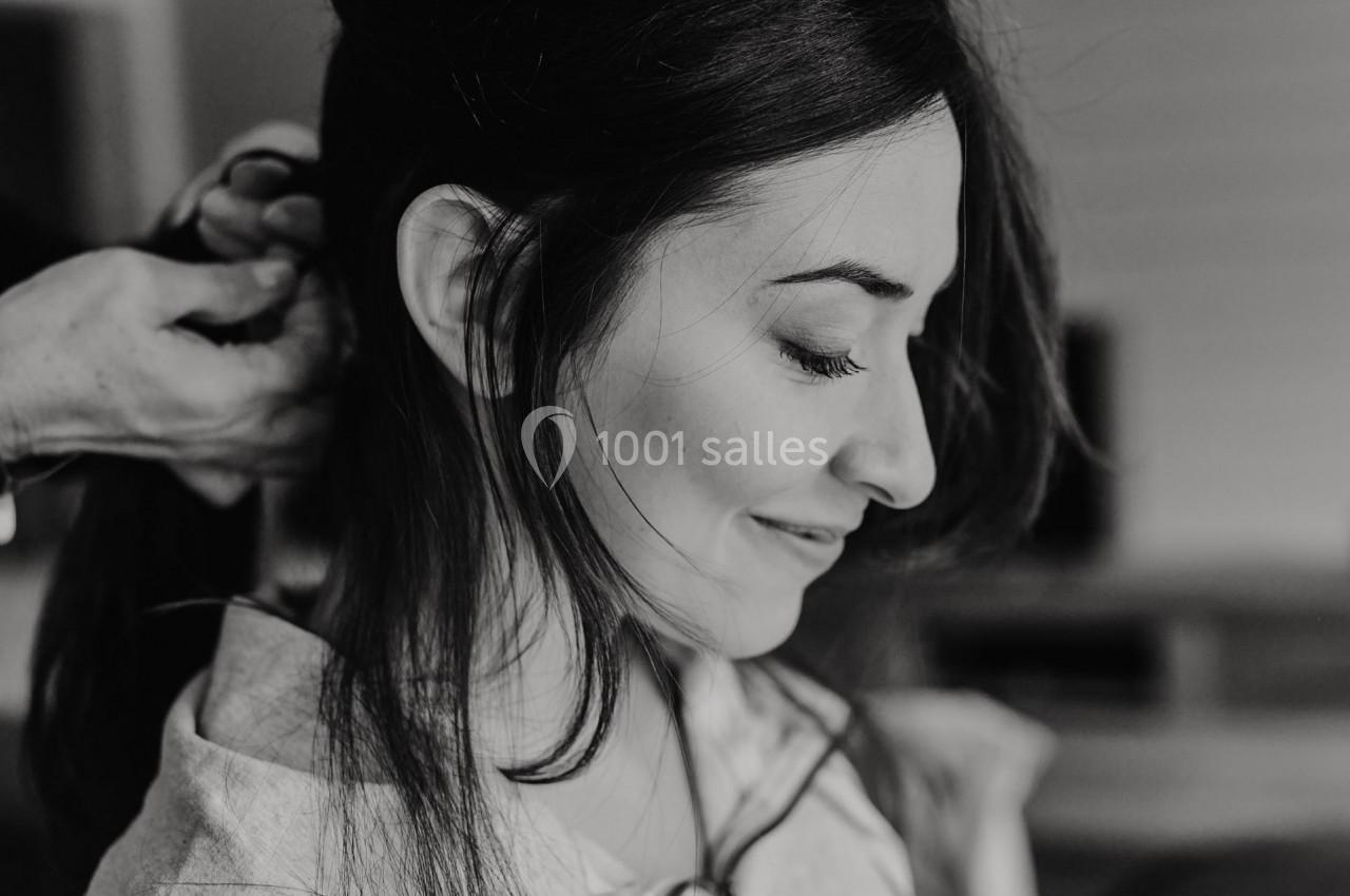 Femme souriante de profil, cheveux attachés par une autre personne dans un cadre intérieur.