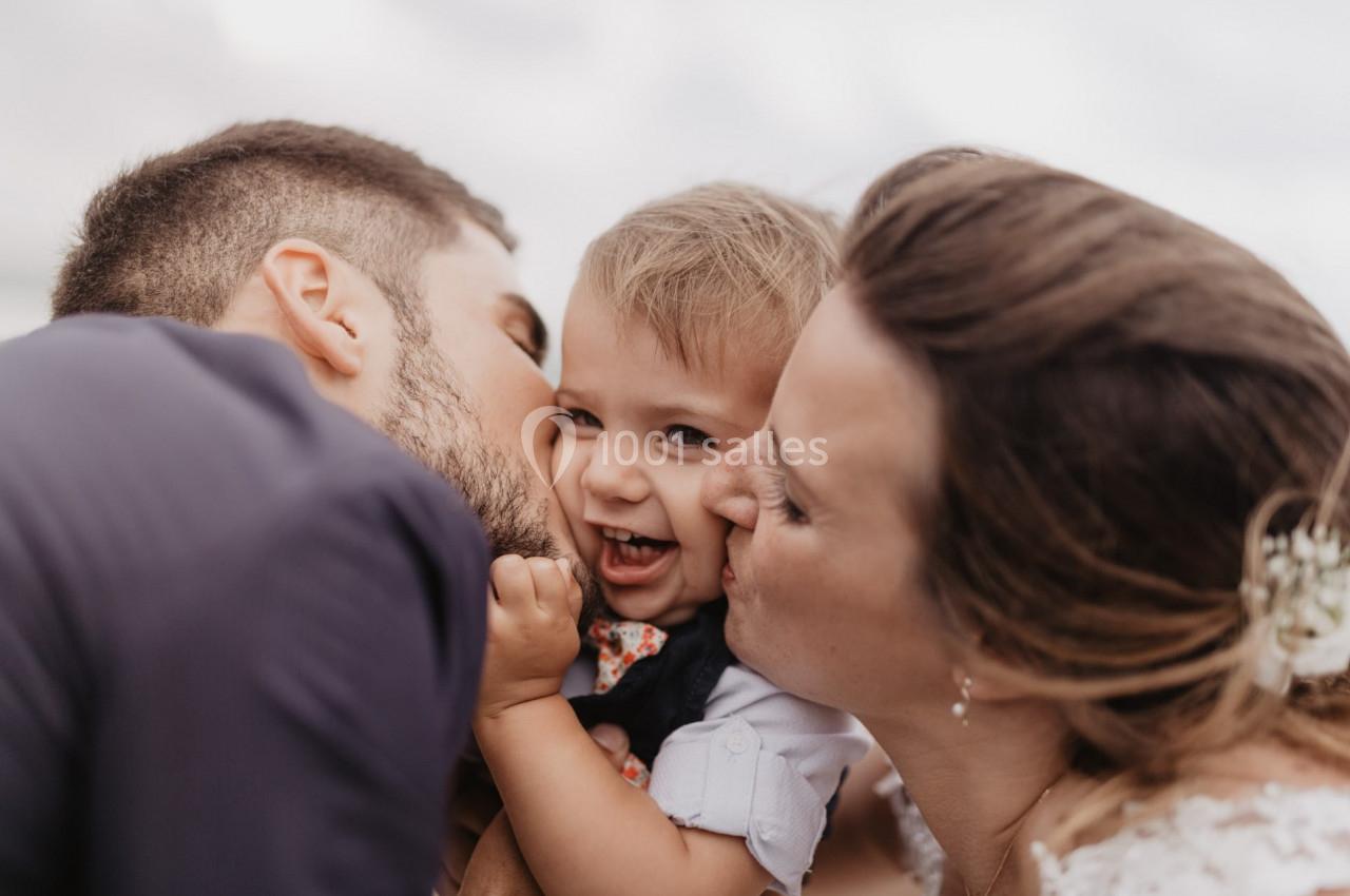 Un couple embrasse tendrement un jeune enfant souriant dans un moment de complicité en extérieur.