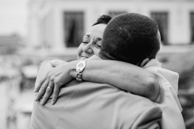 Un couple assis lors d'une cérémonie, l'homme ému essuie une larme tandis que la femme le regarde avec tendresse.