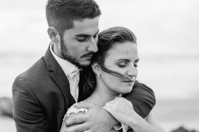 Un couple assis lors d'une cérémonie, l'homme ému essuie une larme tandis que la femme le regarde avec tendresse.