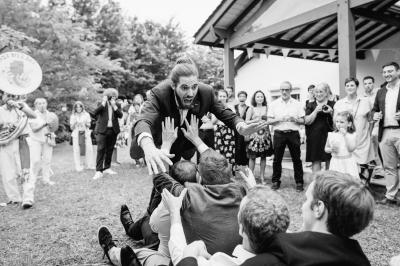 Un couple assis lors d'une cérémonie, l'homme ému essuie une larme tandis que la femme le regarde avec tendresse.