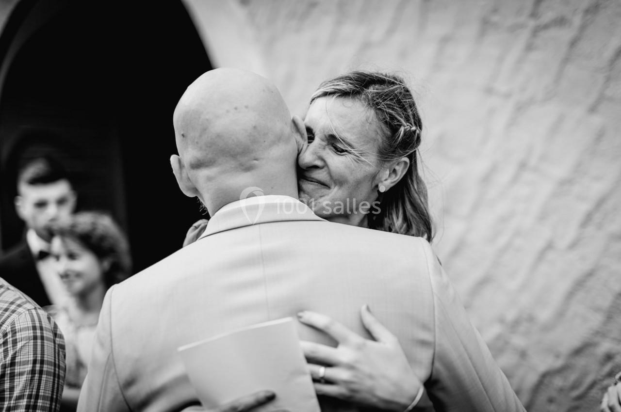 Un homme et une femme s’enlacent chaleureusement lors d’un moment émouvant, en extérieur devant un bâtiment.