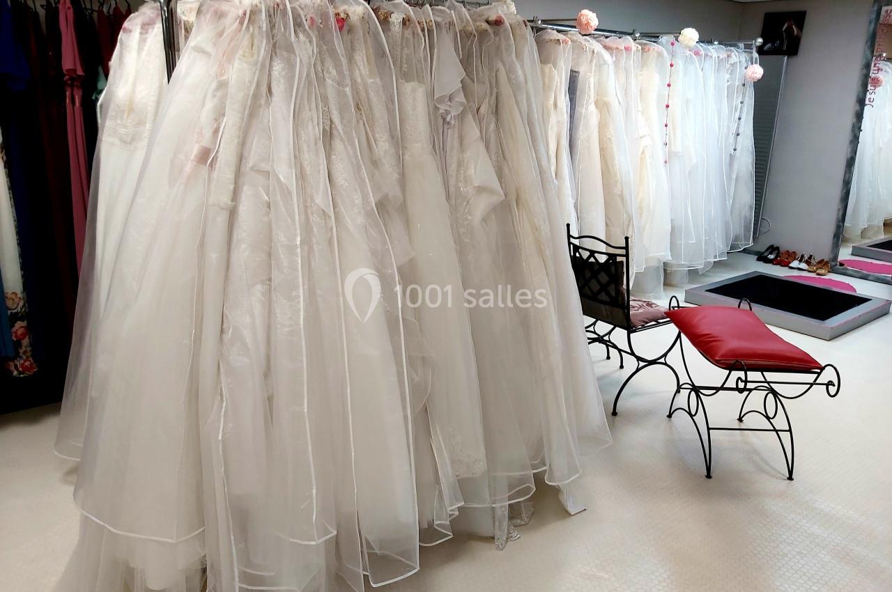Racks de robes de mariée blanches protégées par des housses transparentes dans un showroom lumineux.
