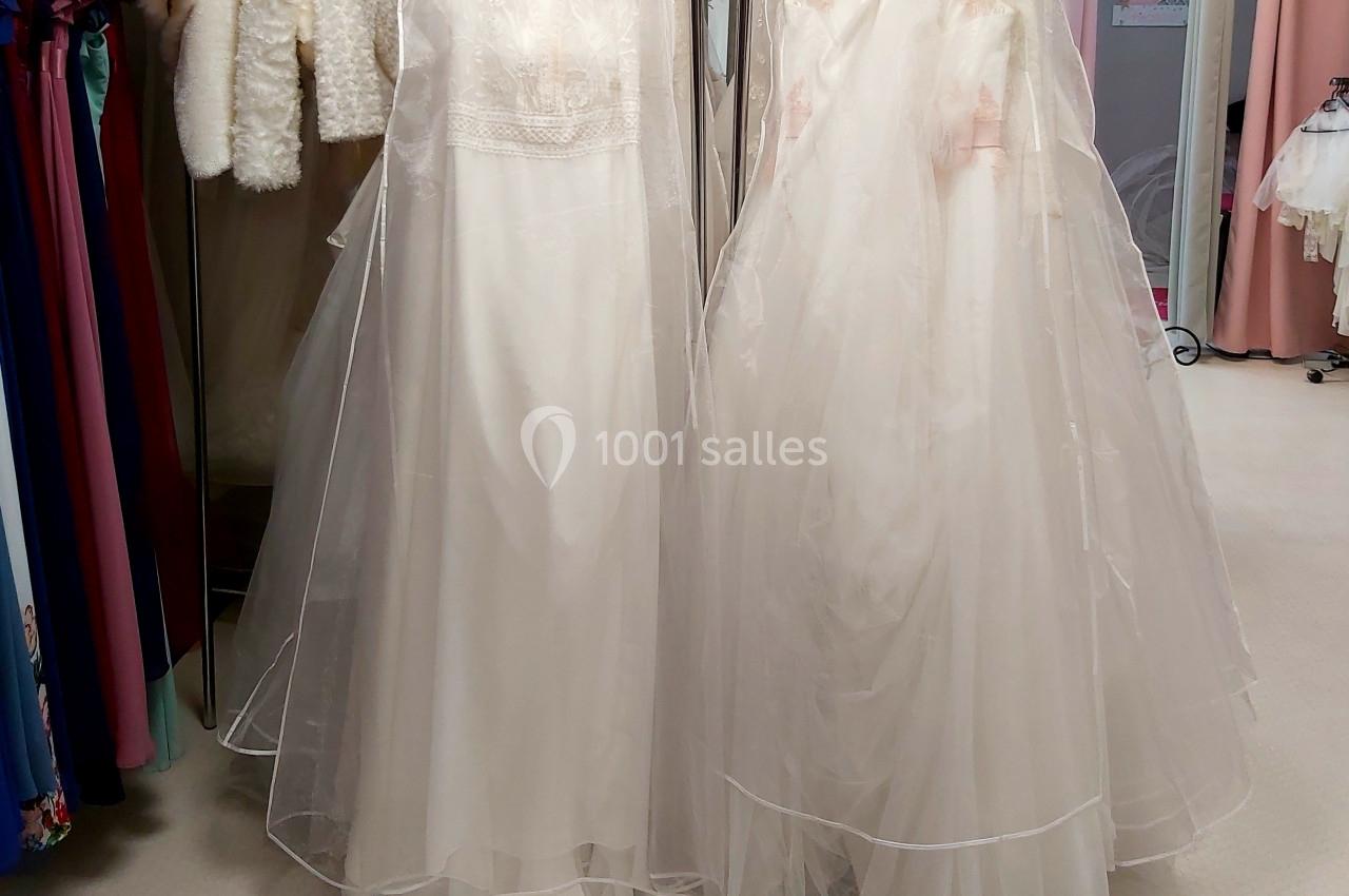 Deux robes de mariée blanches avec voiles transparents suspendues sur des cintres dans une boutique.