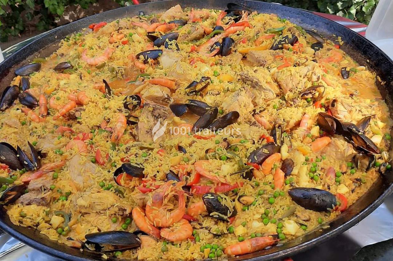 Grande poêle de paella garnie de riz, crevettes, moules, morceaux de viande, légumes et épices.