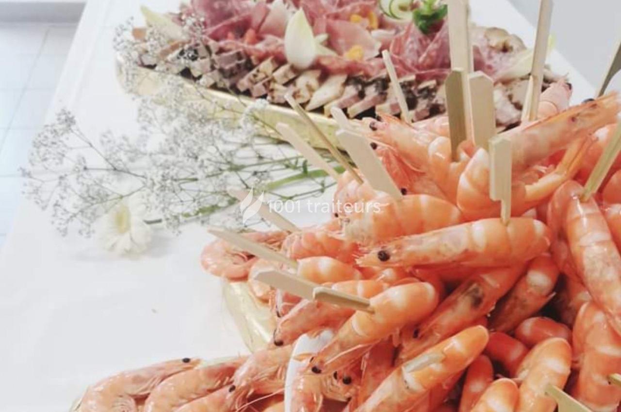 Plateau de crevettes roses présentées avec des piques en bois, accompagné d'un assortiment de charcuteries en arrière-plan.