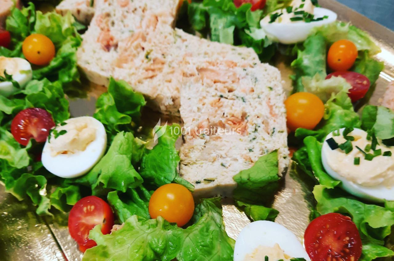 Terrine de poisson entourée de feuilles de salade, tomates cerises, œufs durs garnis et ciboulette sur un plateau doré.