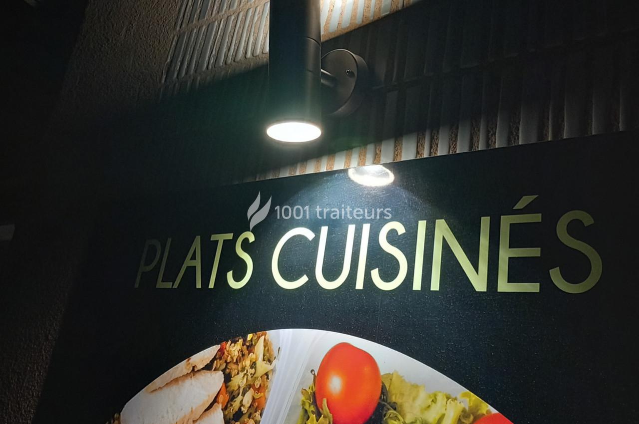 Lampe murale éclairant une enseigne indiquant ’Plats cuisinés’ avec des images de plats en arrière-plan.