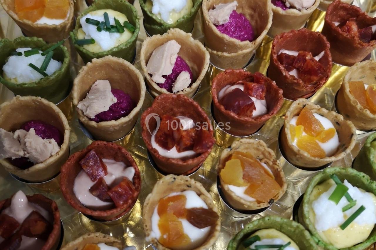 Assortiment de mini-cornets colorés garnis de mousse, légumes, fromage et herbes fraîches, présenté sur un plateau.