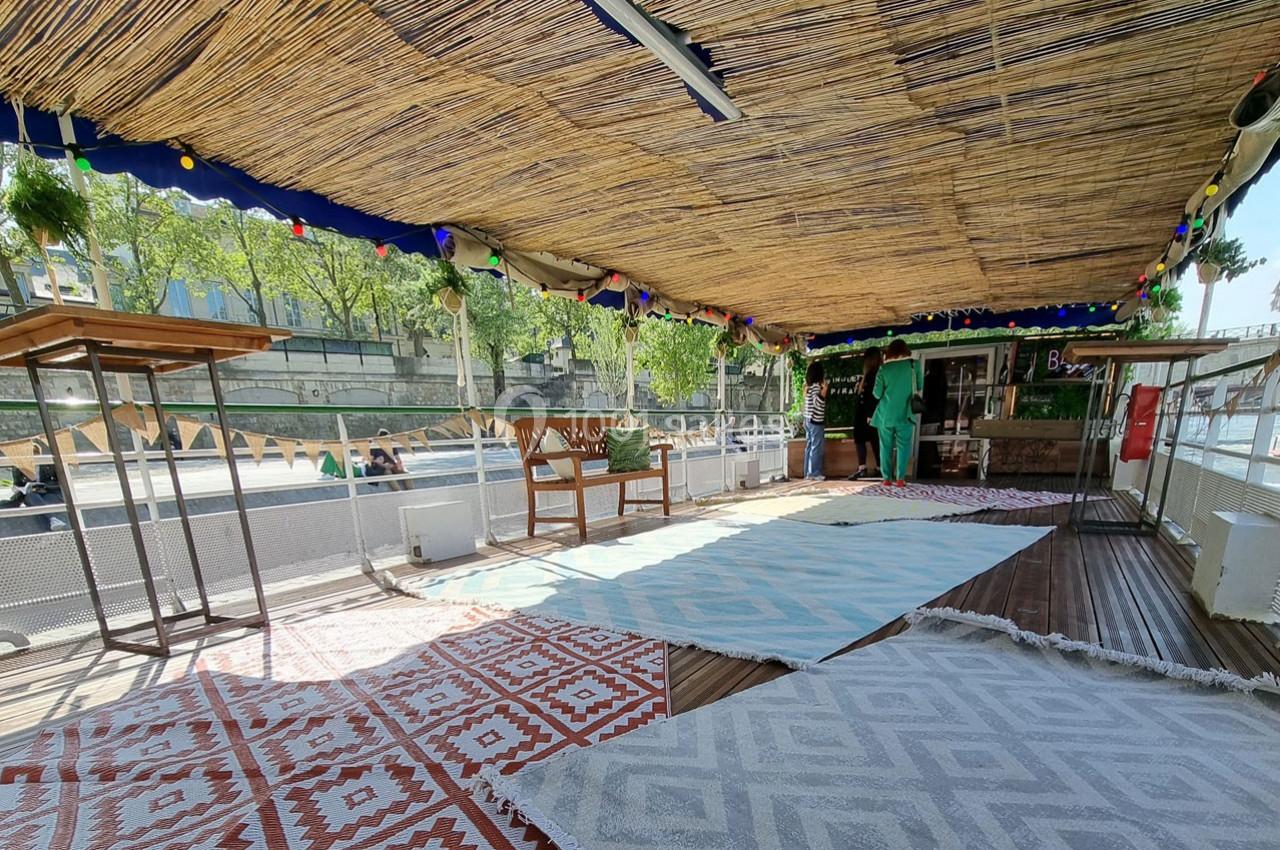 Terrasse couverte en bord de Seine avec tapis colorés, mobilier en bois et décoration végétale.