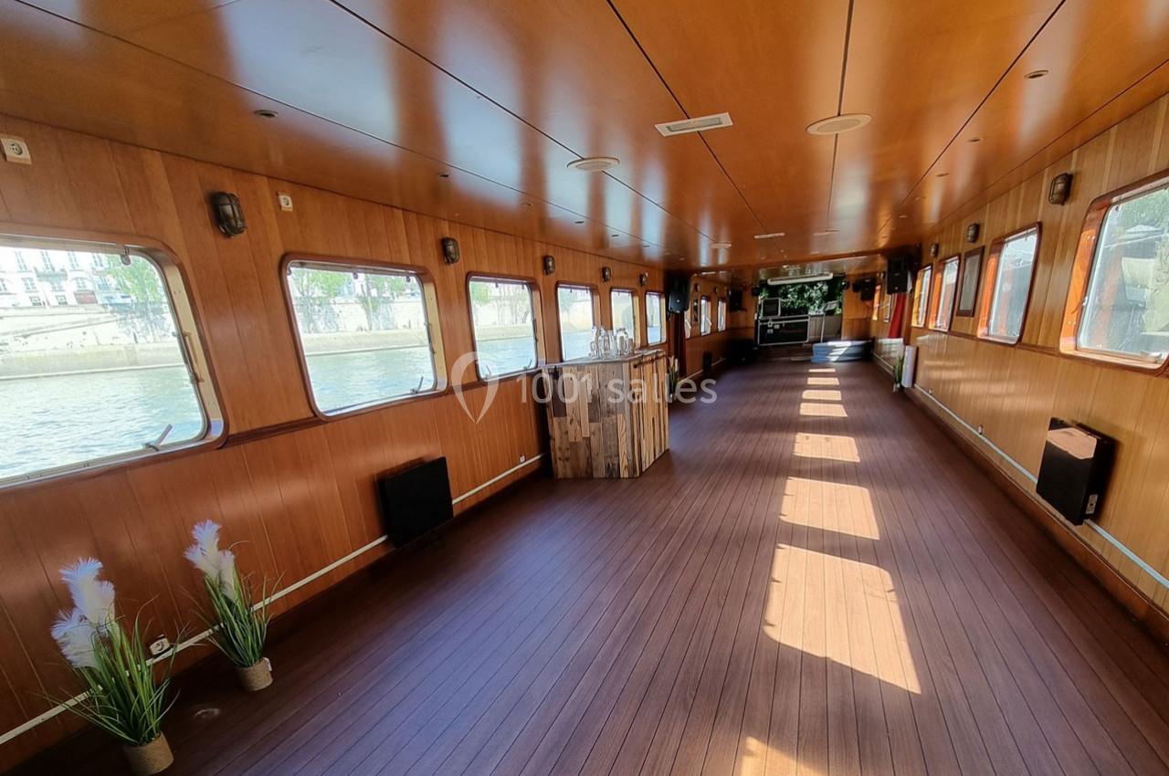 Intérieur d'une péniche avec un sol en bois, des murs lambrissés, des fenêtres donnant sur l'eau et une décoration sobre.