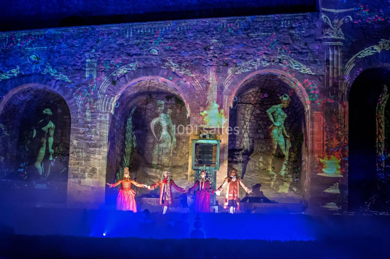 Spectacle nocturne avec projections lumineuses sur des arches en pierre, mettant en scène des artistes costumés.