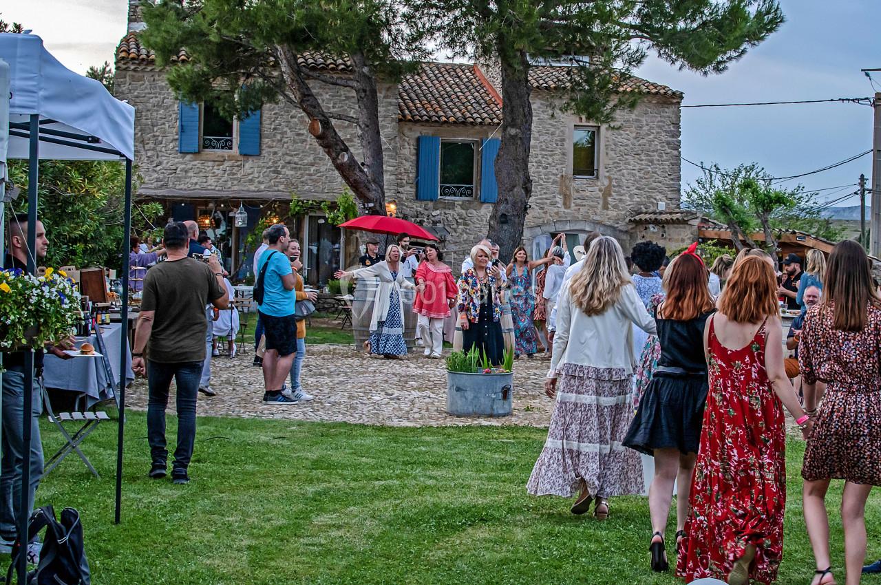 Groupe de personnes rassemblées dans un jardin devant une maison en pierre, lors d'un événement en plein air.
