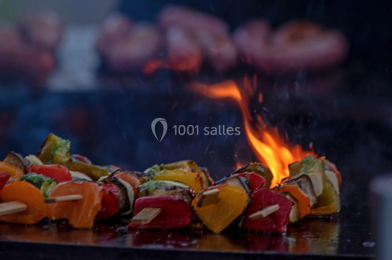 Brochettes de légumes colorés grillant sur une plaque chaude avec des flammes en arrière-plan.