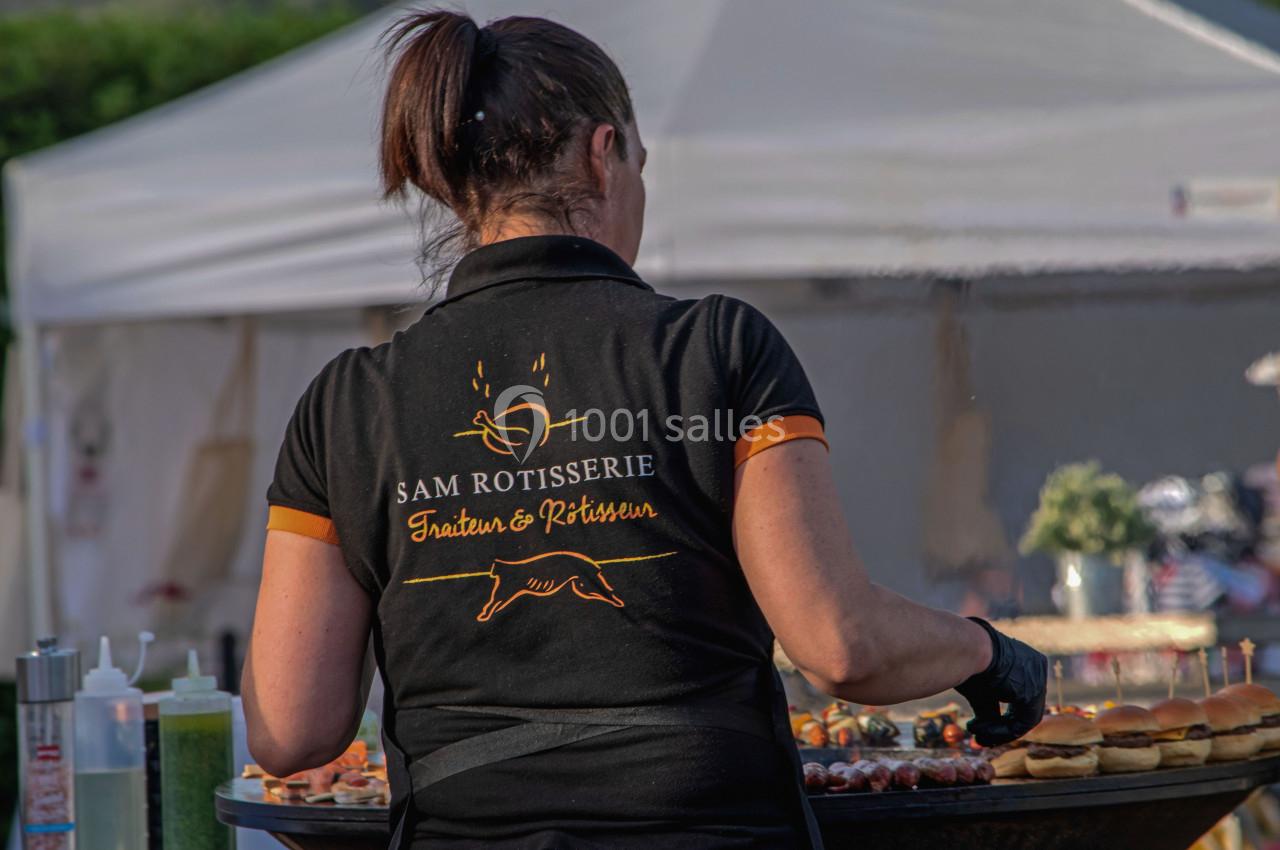 Une femme en tenue professionnelle cuisine devant une grande plancha lors d'un événement en extérieur.