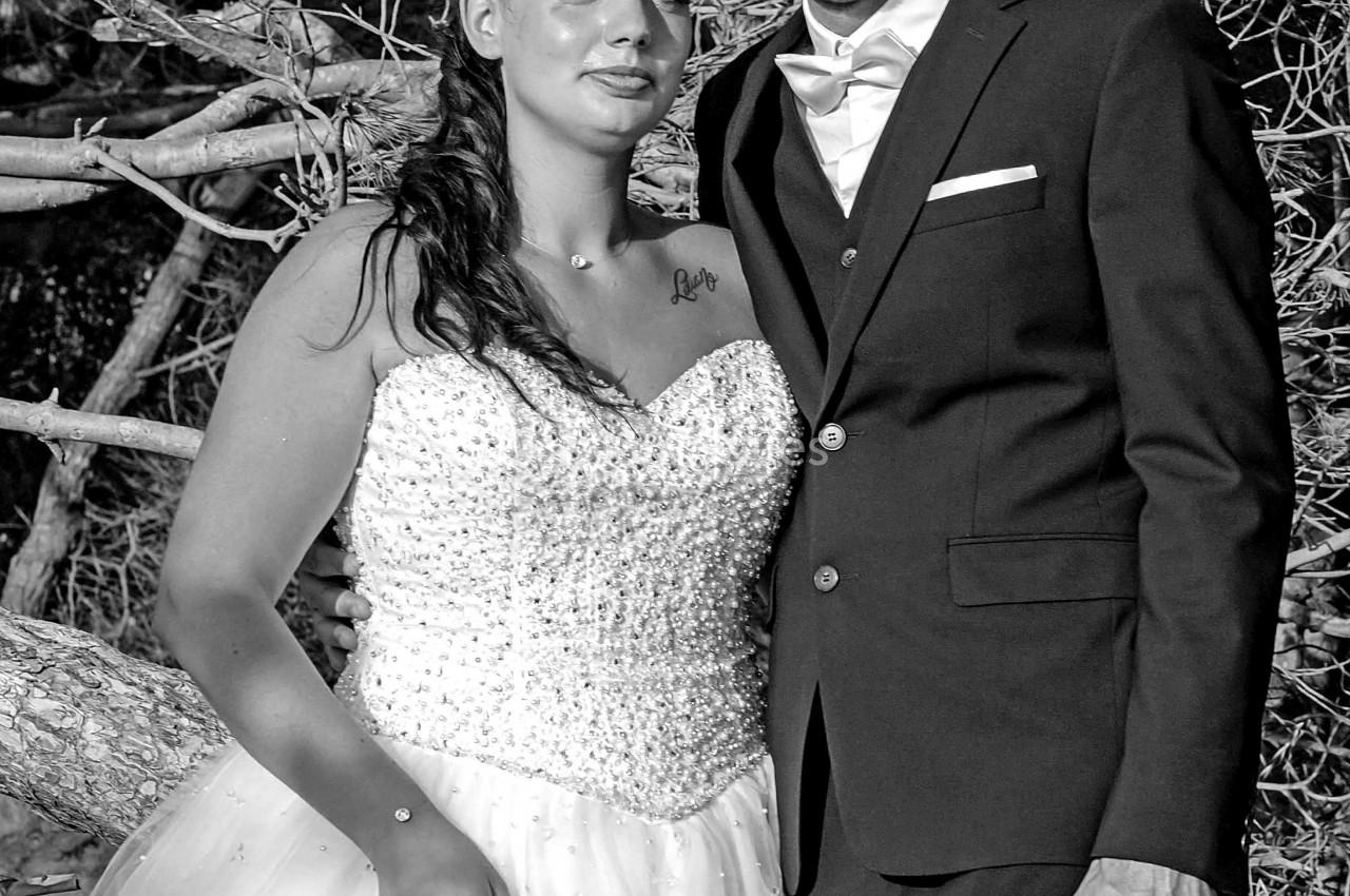 Un couple en tenue de mariage pose devant un arbre dans un cadre naturel, en noir et blanc.