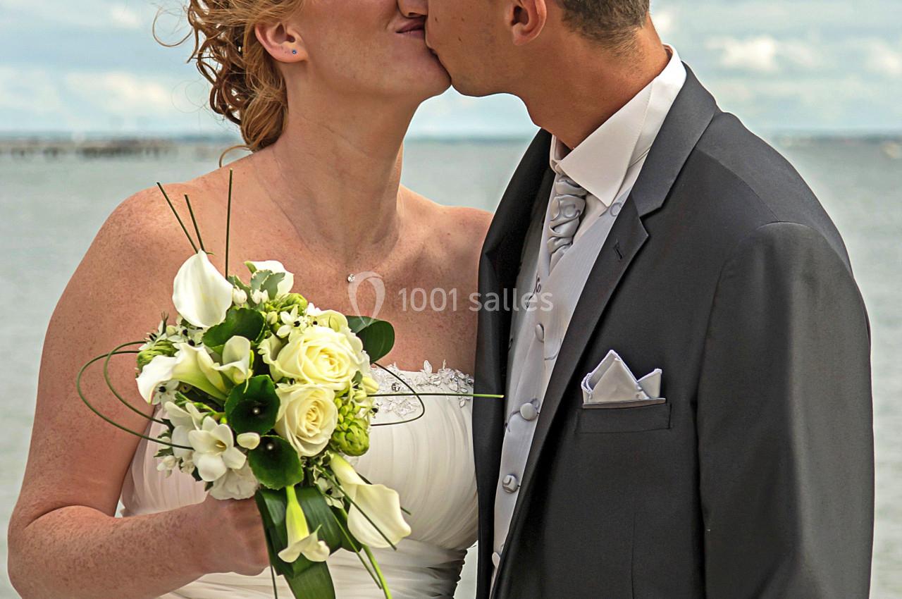 Un couple de mariés s'embrassant près d'un plan d'eau, la mariée tenant un bouquet de fleurs blanches.