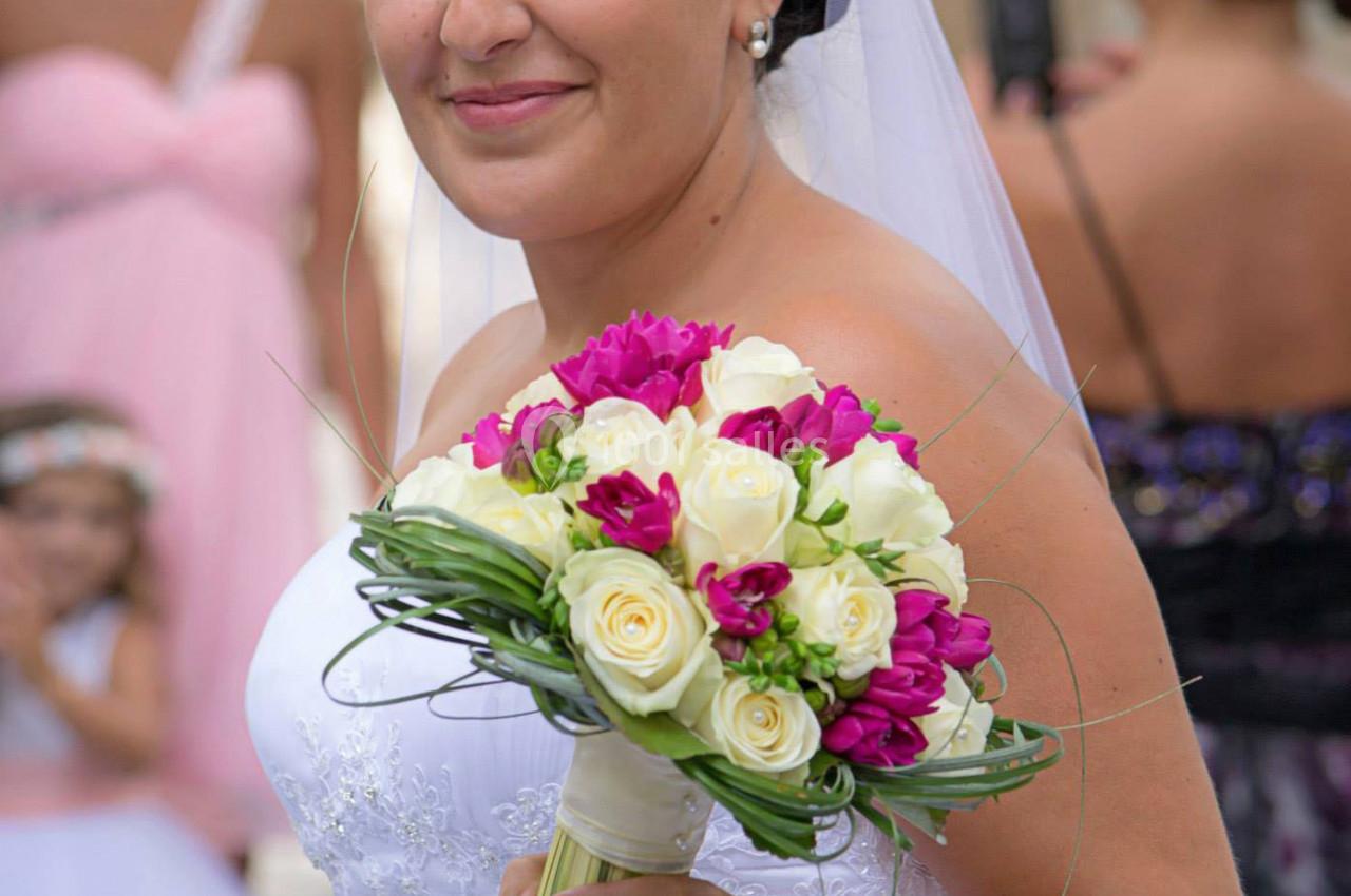 Une mariée en robe blanche tient un bouquet de fleurs blanches et roses lors d'une cérémonie en extérieur.