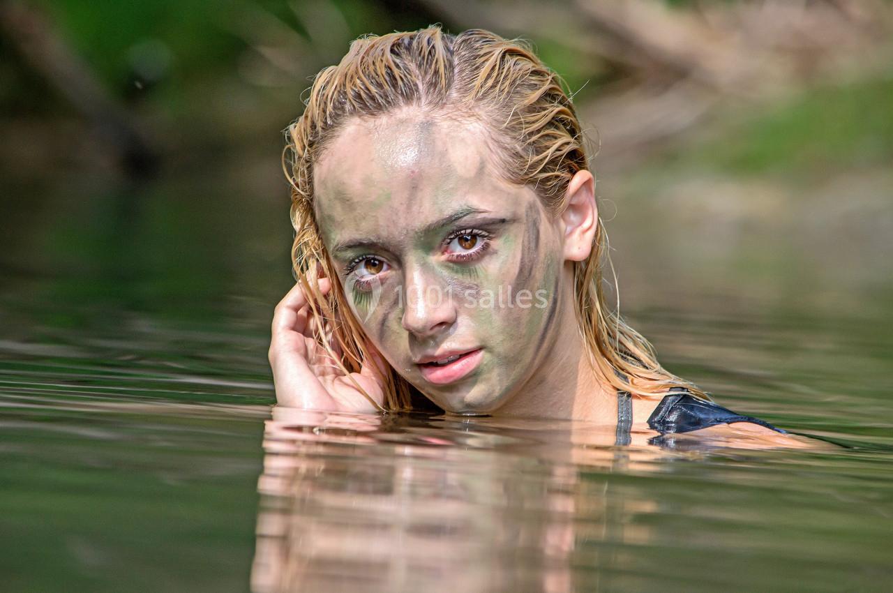 Femme au visage camouflé émergeant partiellement de l'eau dans un environnement naturel.