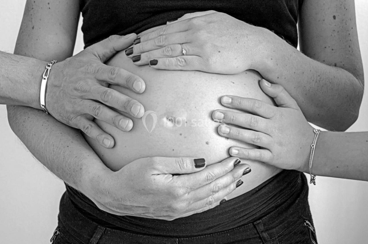 Des mains posées sur un ventre rond de femme enceinte, symbolisant le soutien et la connexion familiale.