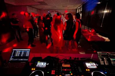 Vue depuis une table de mixage sur un groupe de personnes dansant dans une salle éclairée par une lumière rouge.