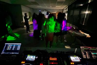 Vue depuis une table de mixage sur un groupe de personnes dansant dans une salle éclairée par une lumière rouge.