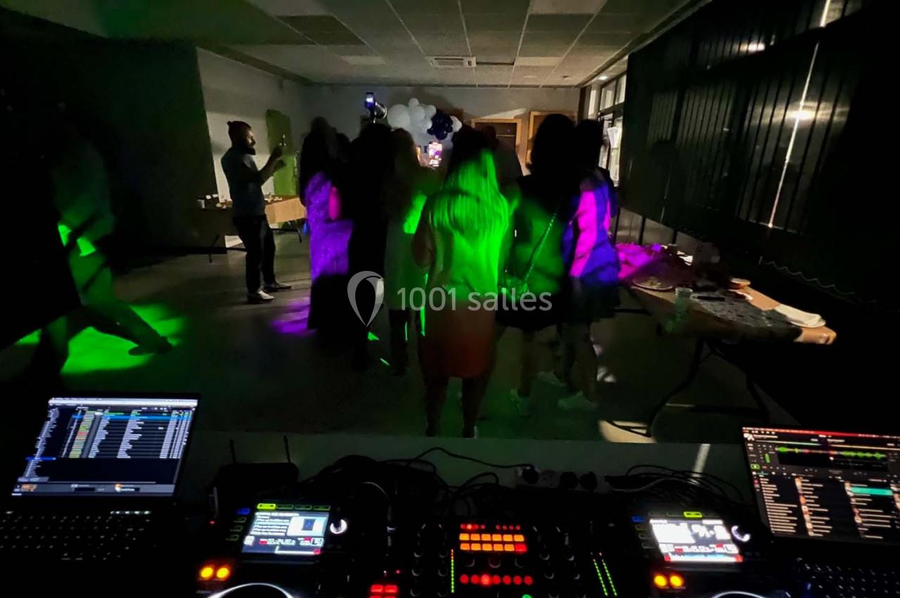Des personnes dansent dans une salle sombre éclairée par des lumières colorées, avec une table de mixage au premier plan.