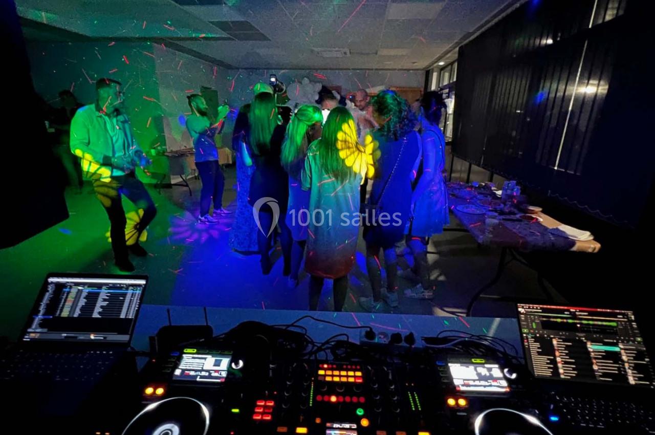 Groupe de personnes dansant dans une salle sombre avec des lumières colorées, vue depuis une table de mixage DJ.