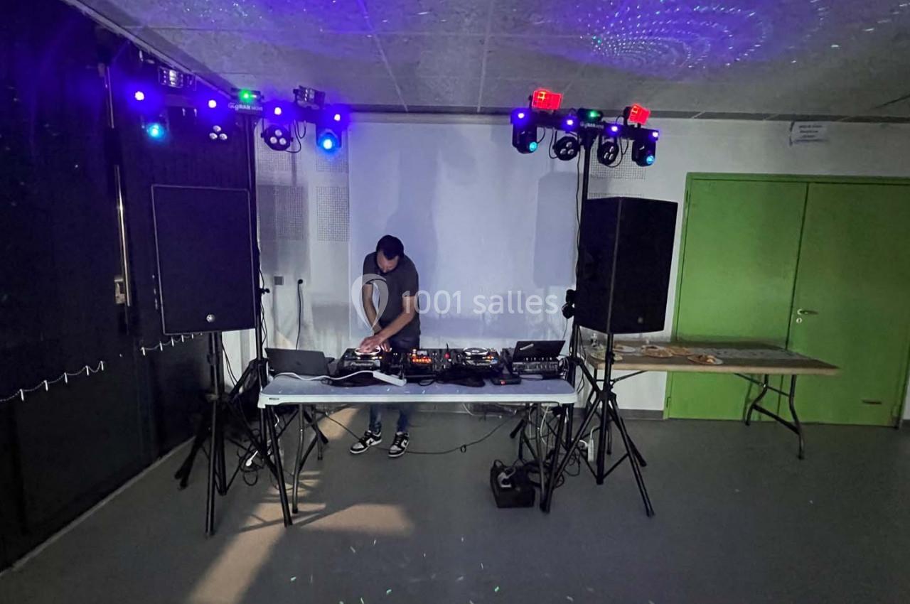 Un DJ mixe sur une table équipée de matériel audio, entouré de lumières colorées dans une salle sombre.