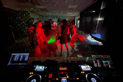 Vue depuis une table de mixage sur un groupe de personnes dansant dans une salle éclairée par une lumière rouge.
