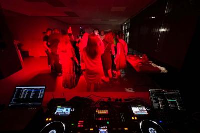 Vue depuis une table de mixage sur un groupe de personnes dansant dans une salle éclairée par une lumière rouge.