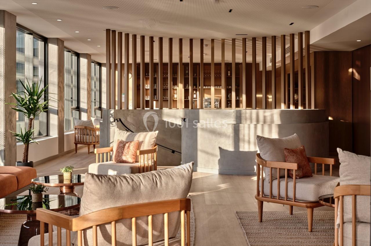 Espace lumineux avec fauteuils en bois, tables basses et parois vitrées, offrant une ambiance chaleureuse et moderne.