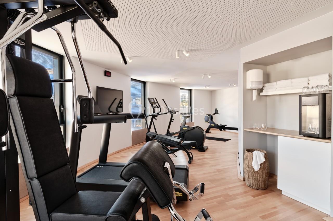 Salle de sport lumineuse avec équipements de musculation, vélos d'exercice et coin avec fontaine à eau.