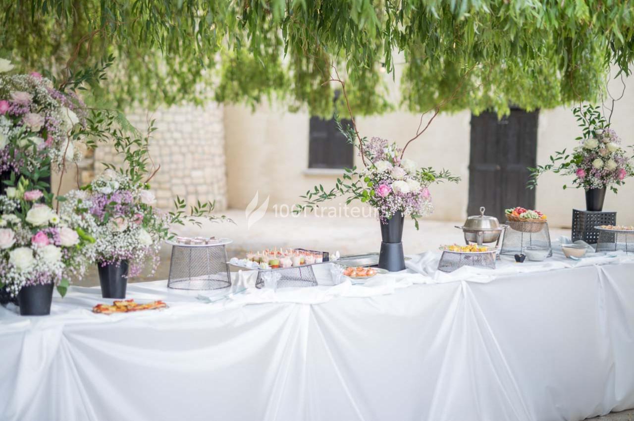 Table de buffet décorée de fleurs et plats variés, installée en extérieur sous des branches d'arbres.