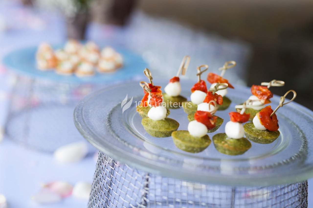 Assortiment de bouchées apéritives avec tomates, mozzarella et base verte, présentées sur un plateau en verre.