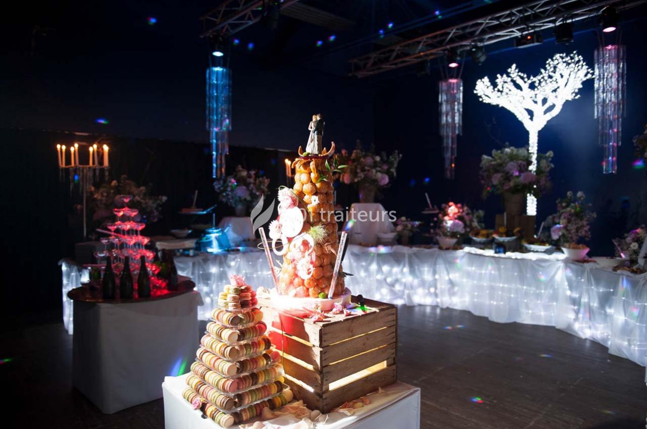 Dessert de fête avec une pièce montée, une pyramide de macarons et une décoration lumineuse dans une salle sombre.