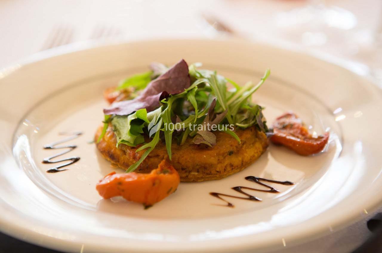 Plat végétarien composé d'une galette de légumes, de feuilles de salade et de tomates rôties, décoré de sauce balsamique.
