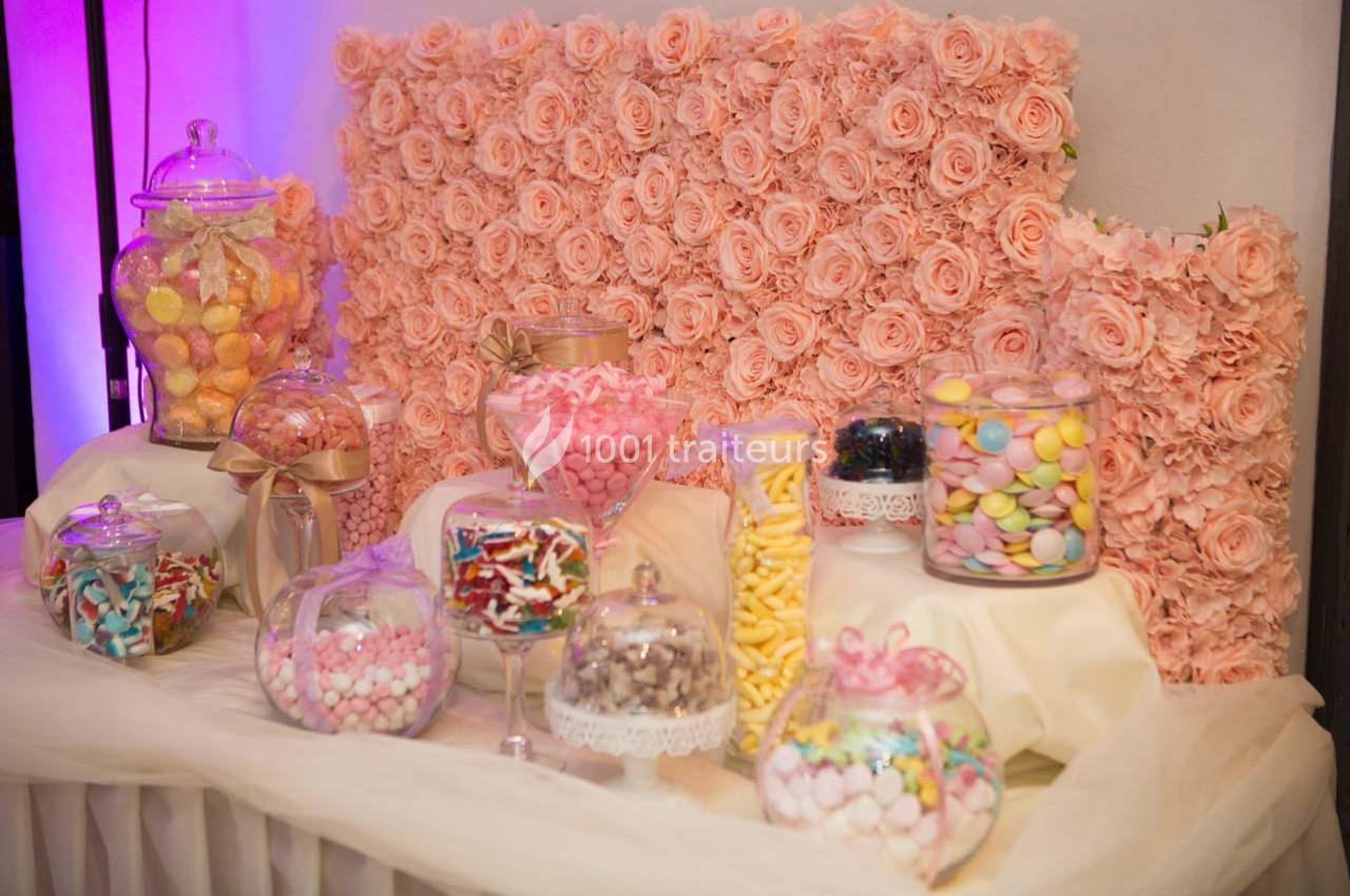 Table décorative avec des bonbonnières remplies de sucreries colorées, entourées de roses roses en arrière-plan.