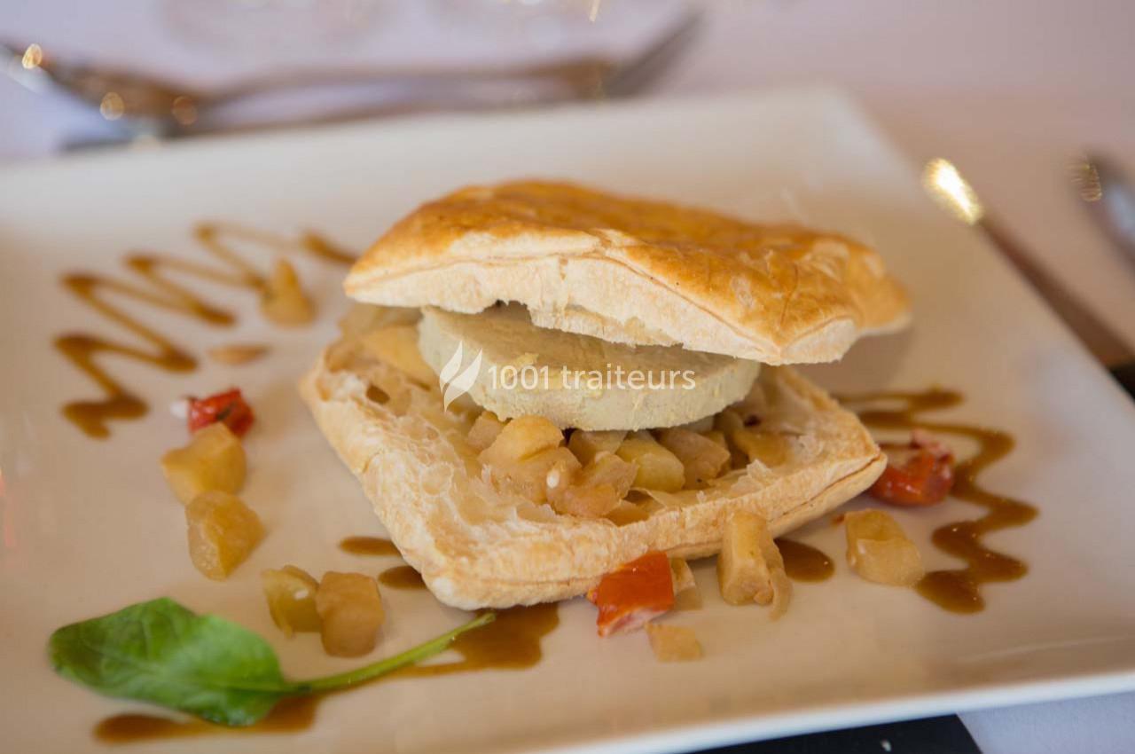 Feuilleté garni de foie gras et compotée de pommes, accompagné de sauce décorative et de légumes sur une assiette blanche.