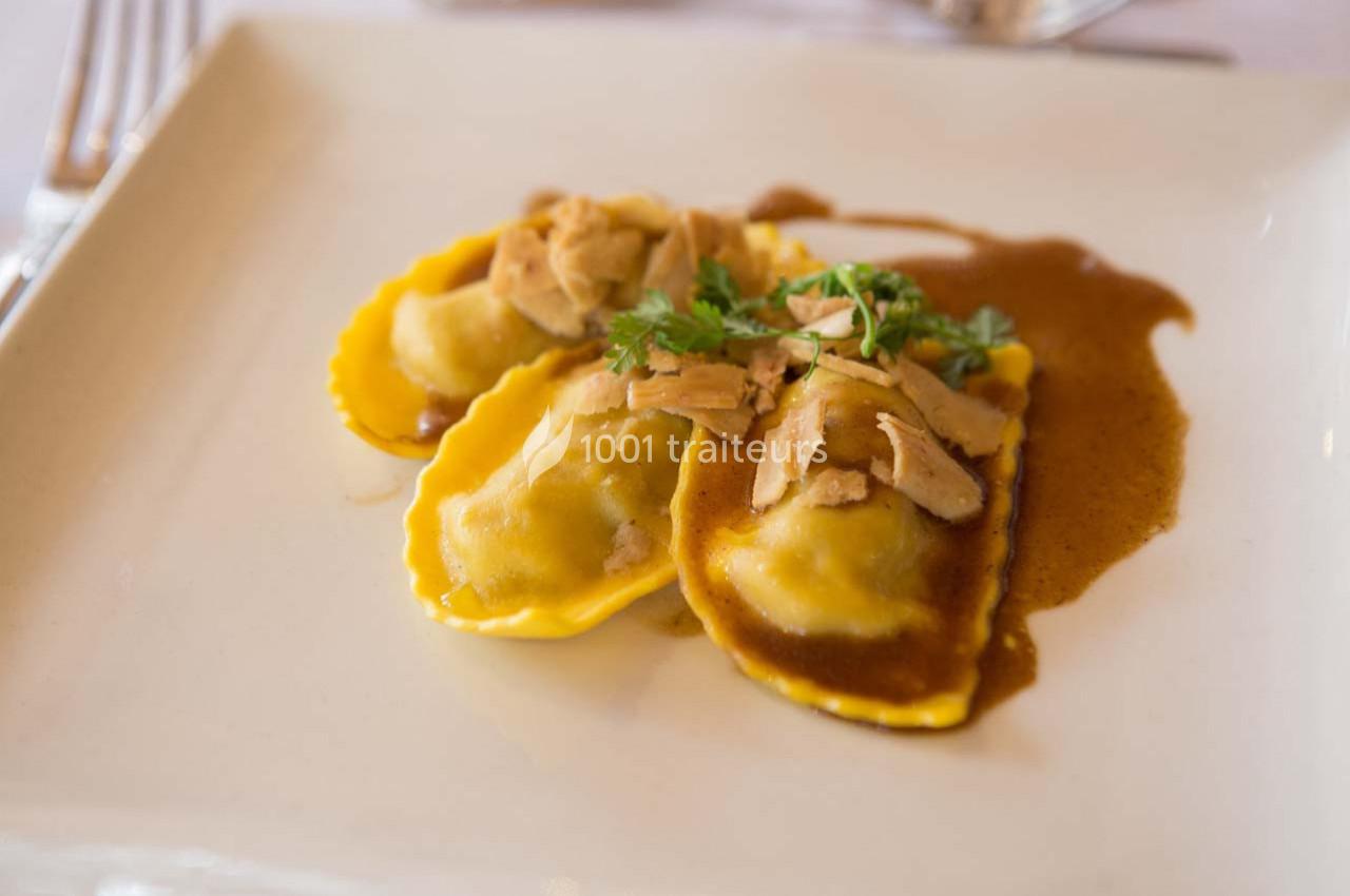Assiette de raviolis garnis, nappés de sauce brune, garnis de morceaux de viande et de persil frais.