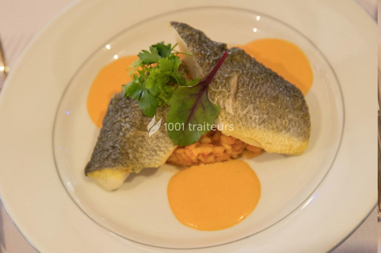 Filet de poisson grillé servi sur un lit de risotto avec une sauce orange et une garniture de feuilles vertes.
